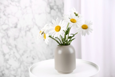 Photo of Beautiful tender chamomile flowers in vase on white table indoors