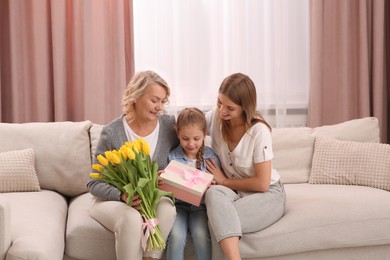 Little girl congratulating her mom and granny with flowers and gift at home. Happy Mother's Day