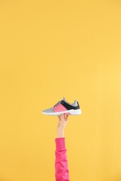 Woman holding sportive shoe on yellow background, closeup. Space for text