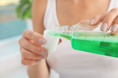 Photo of Woman pouring mouthwash from bottle into cap, closeup. Teeth care