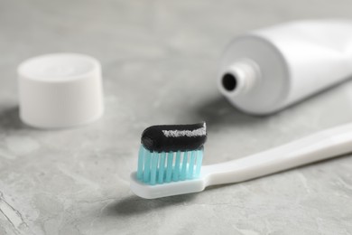 Photo of Brush with charcoal toothpaste on light grey table, closeup