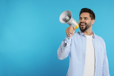 Photo of Special promotion. Smiling man with megaphone on light blue background. Space for text