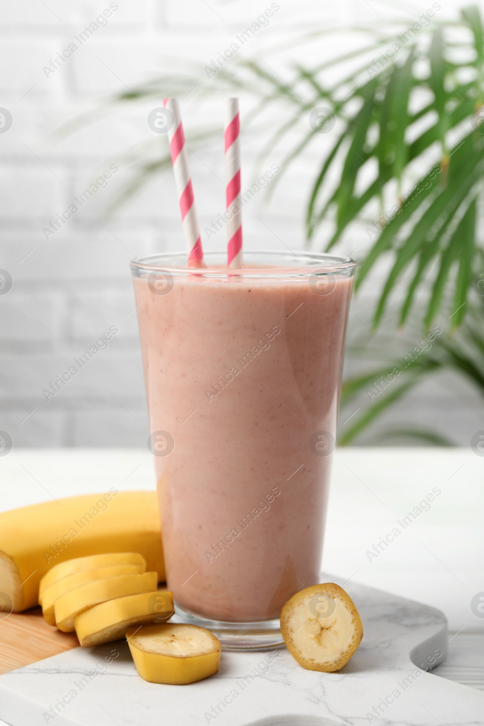 Photo of Glass of tasty banana smoothie with straws and fresh fruit on white wooden table