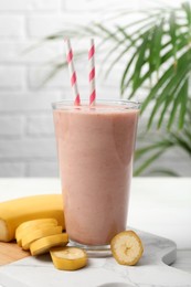 Glass of tasty banana smoothie with straws and fresh fruit on white wooden table