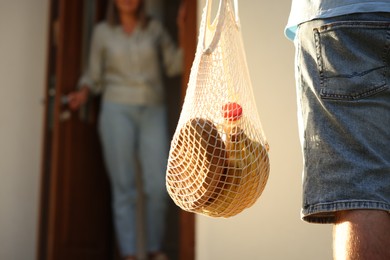 Photo of Helping neighbours. Man with net bag of products visiting senior woman outdoors, closeup