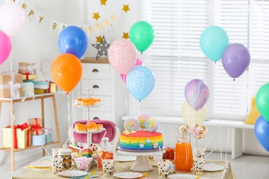 Photo of Bright birthday cake and other treats on table in decorated room