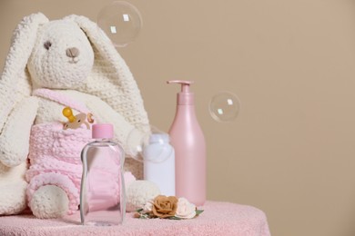 Photo of Baby cosmetic products, toy bunny, accessories and soap bubbles on beige background. Space for text