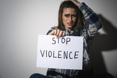 Photo of Crying young woman with sign STOP VIOLENCE near white wall