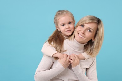 Daughter hugging her happy mother on light blue background