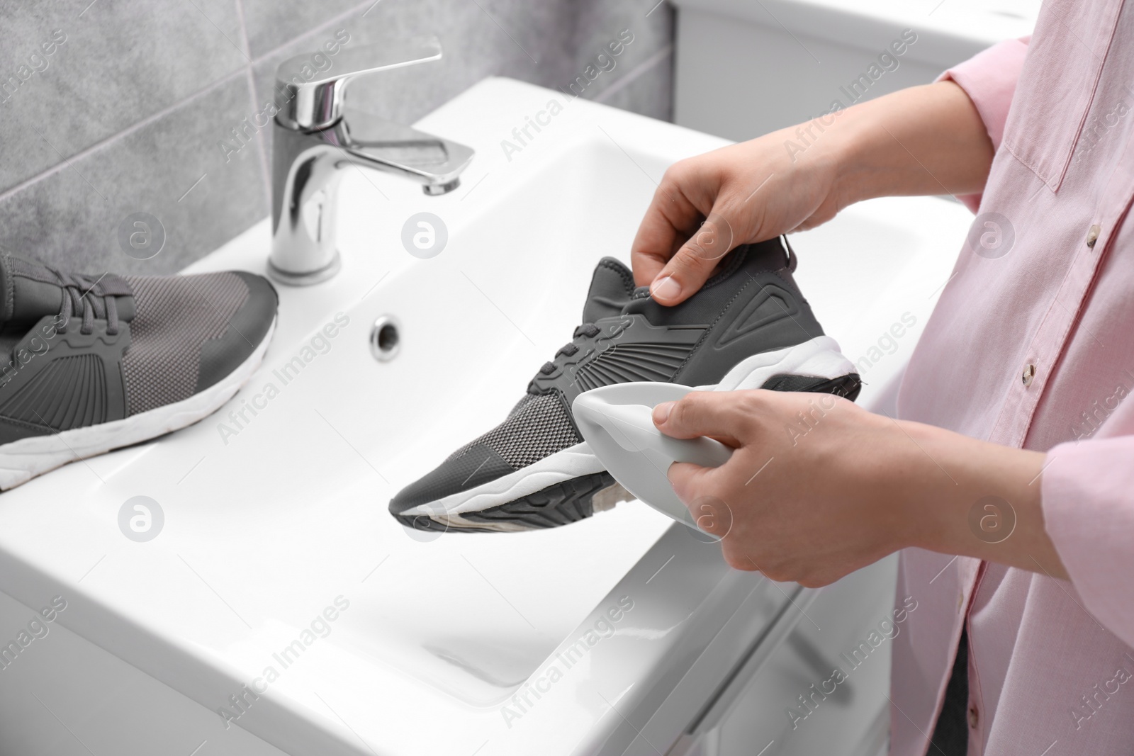 Photo of Woman washing stylish sneakers with brush in sink, closeup