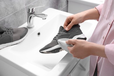 Woman washing stylish sneakers with brush in sink, closeup