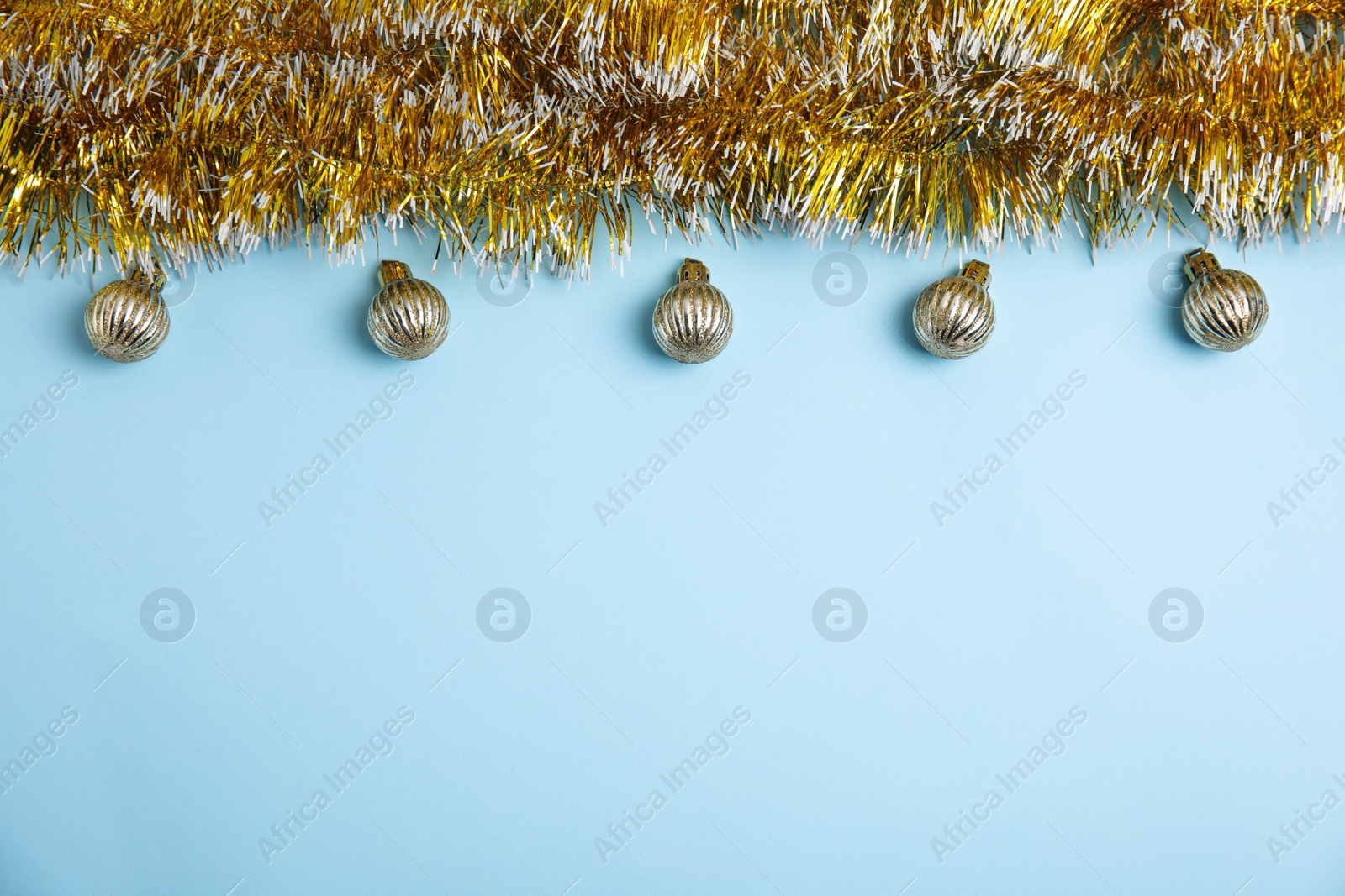 Photo of Golden tinsel and Christmas balls on light blue background, flat lay. Space for text