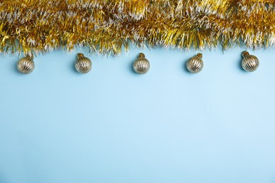 Golden tinsel and Christmas balls on light blue background, flat lay. Space for text