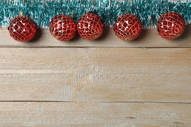 Bright tinsel and Christmas balls on wooden background, flat lay. Space for text