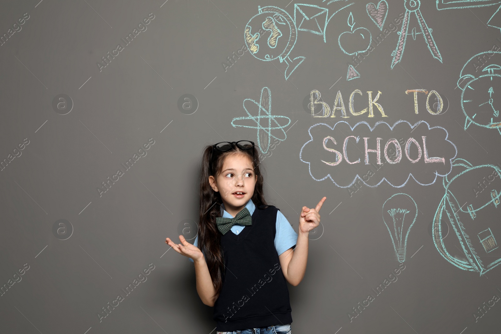 Photo of Little child in uniform near drawings with text BACK TO SCHOOL on grey background