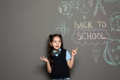 Little child in uniform near drawings with text BACK TO SCHOOL on grey background