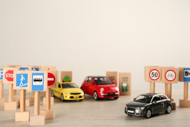 Photo of Many different miniature road signs and cars on wooden table, space for text. Driving school