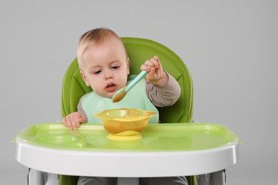 Cute little baby eating healthy food in high chair on gray background