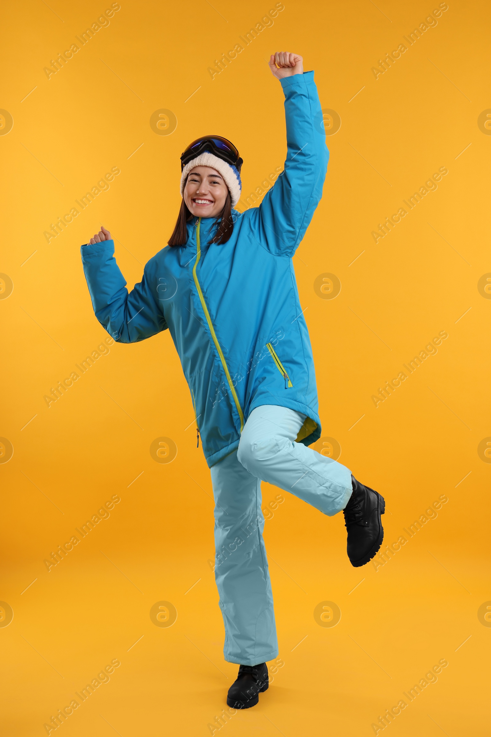 Photo of Winter sports. Happy woman with snowboard goggles on orange background