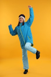 Winter sports. Happy woman with snowboard goggles on orange background