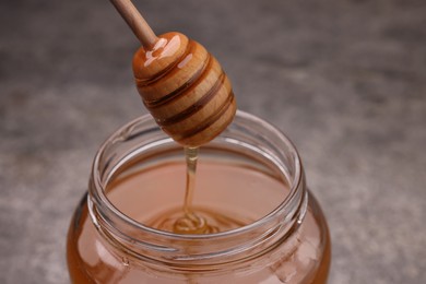 Photo of Pouring sweet golden honey from dipper into jar at table, closeup