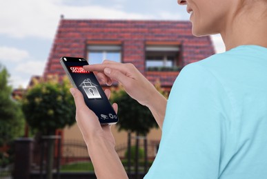 Woman using home security system application on smartphone outdoors, closeup