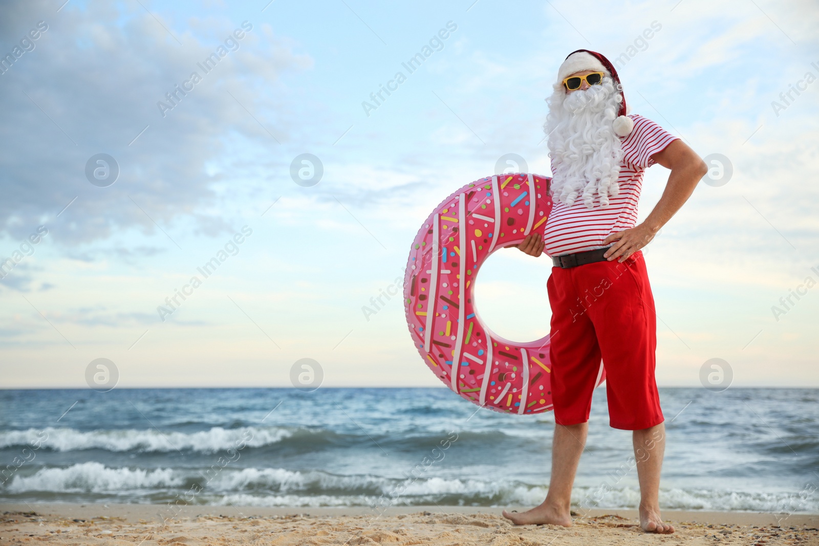 Photo of Santa Claus with inflatable ring on beach, space for text. Christmas vacation