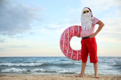 Santa Claus with inflatable ring on beach, space for text. Christmas vacation