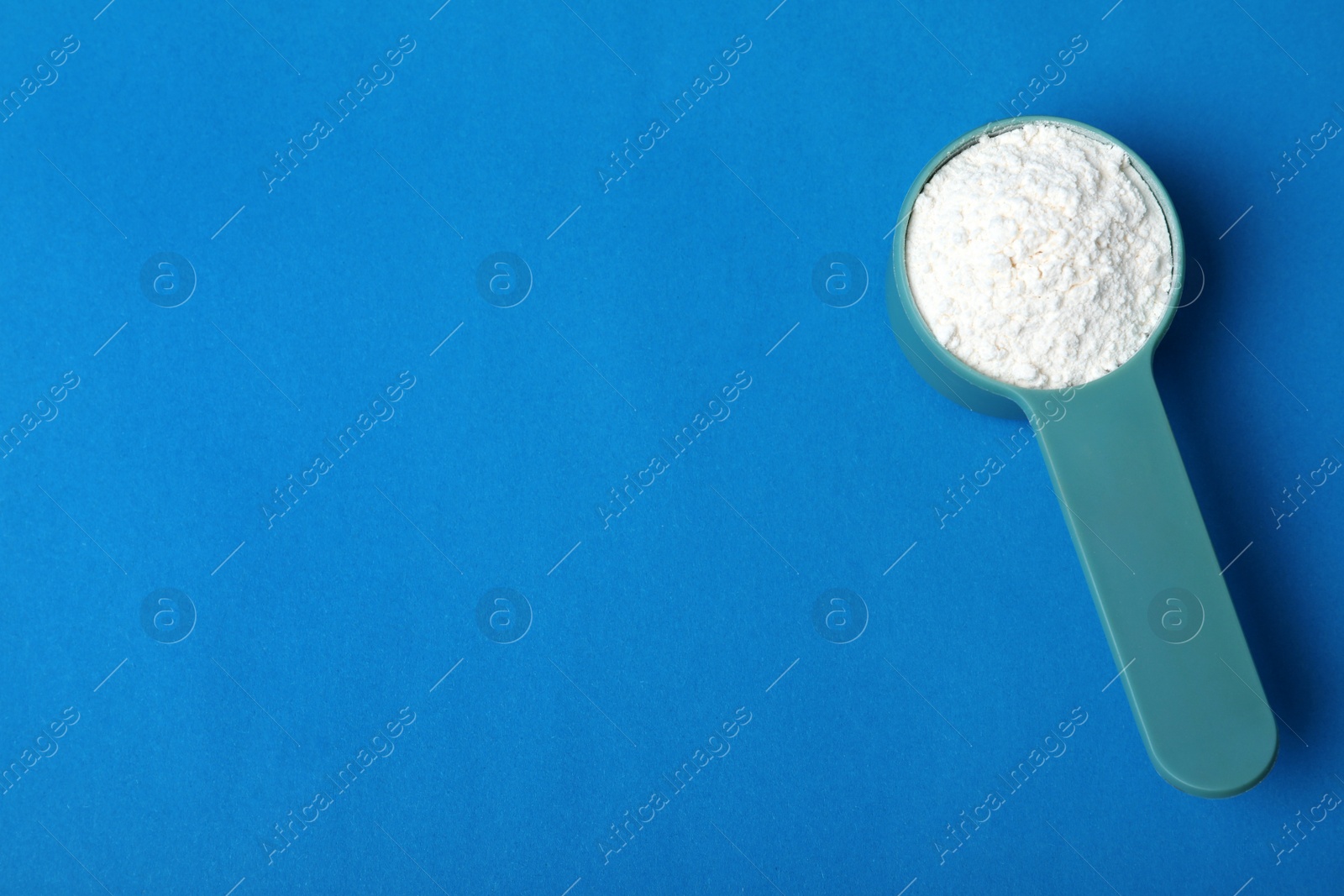 Photo of Scoop of protein powder on blue background, top view with space for text