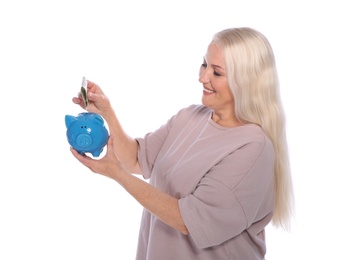 Mature woman putting money into piggy bank on white background