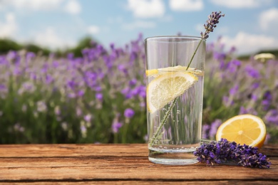 Lemonade with lemon slices and lavender flowers on wooden table outdoors, closeup. Space for text