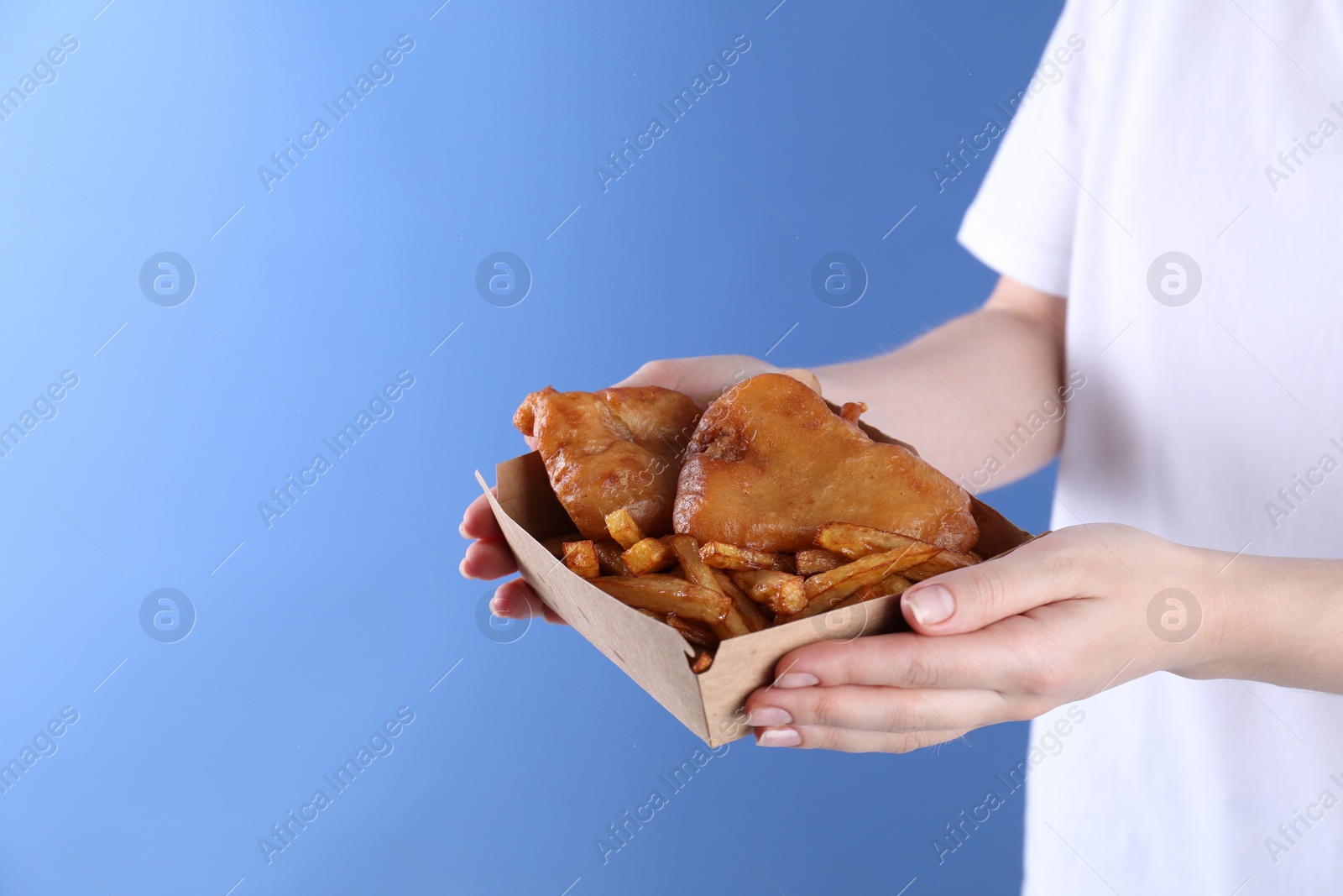 Photo of Woman holding fish and chips in paper box on blue background, closeup. Space for text