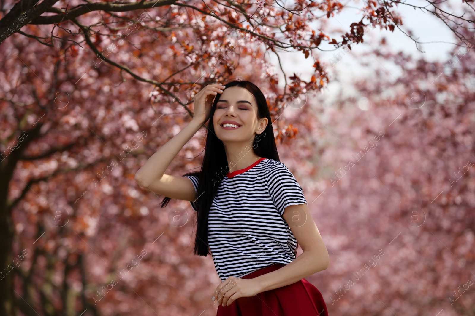 Photo of Pretty young woman wearing trendy clothes near beautiful blossoming trees outdoors. Stylish spring look