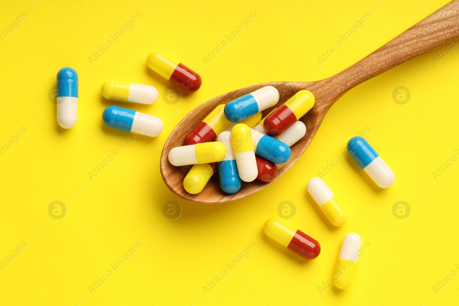 Photo of Antibiotic pills and spoon on yellow background, top view