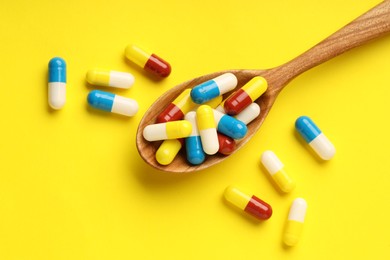 Antibiotic pills and spoon on yellow background, top view