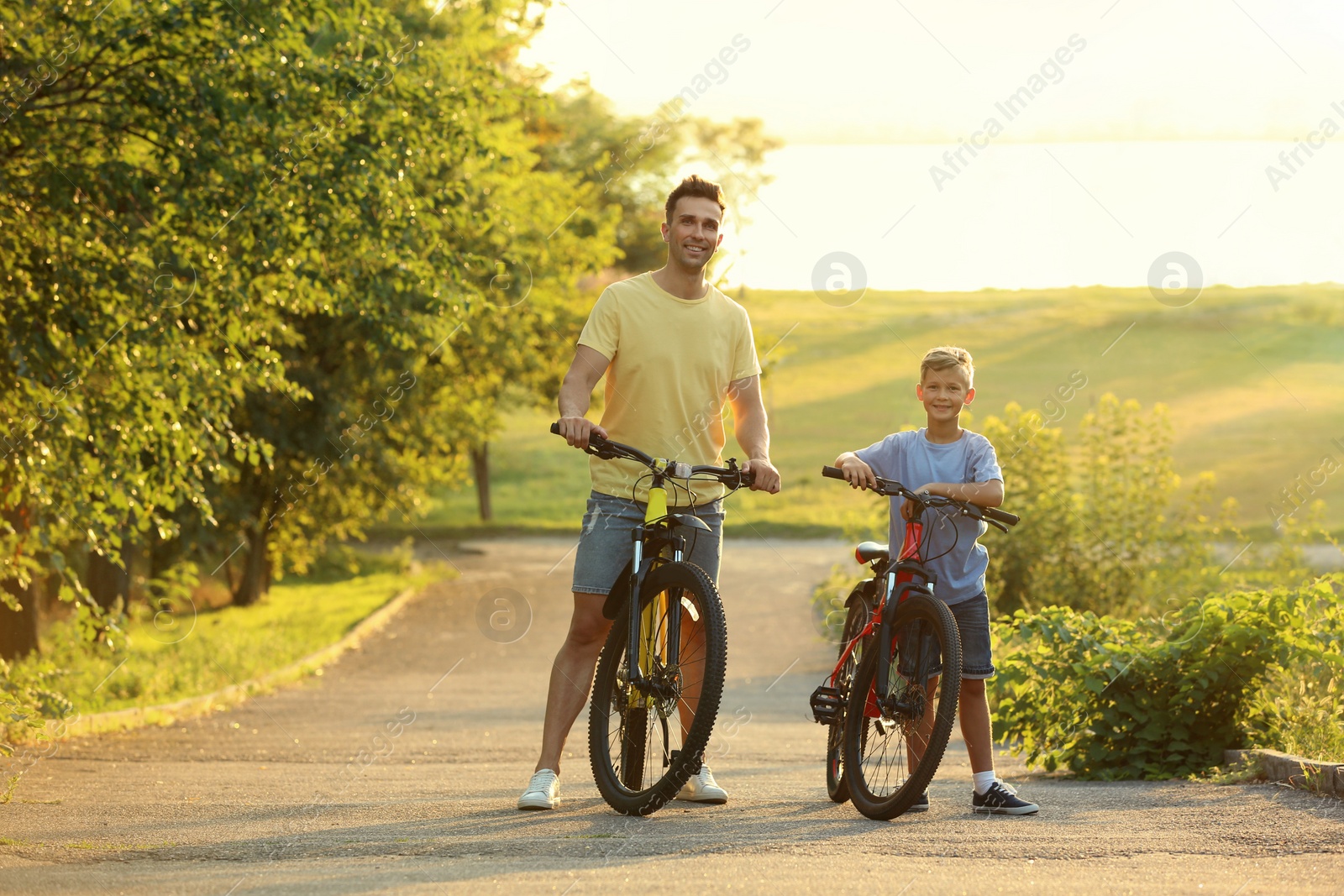 Photo of Dad and son riding bicycles in park on sunny day. Space for text