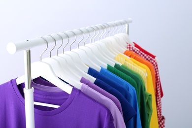 Photo of Rack with rainbow clothes on light background