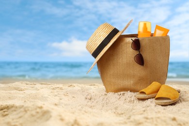 Image of Bag with accessories and cosmetics on sunny ocean beach, space for text. Summer vacation