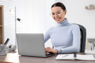 Young woman in glasses watching webinar at table in office