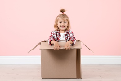 Cute little girl playing with cardboard box near color wall indoors