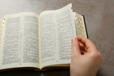 Above view of woman reading Bible at light grey table, closeup