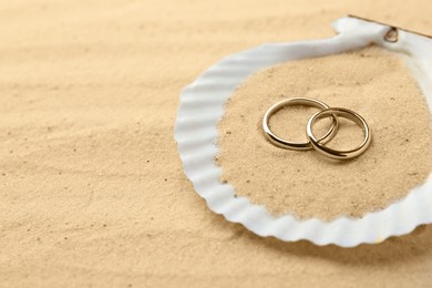 Honeymoon concept. Two golden rings and shell on sand, closeup