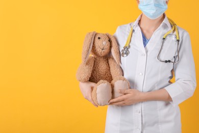 Photo of Pediatrician with toy bunny and stethoscope on yellow background, closeup. Space for text