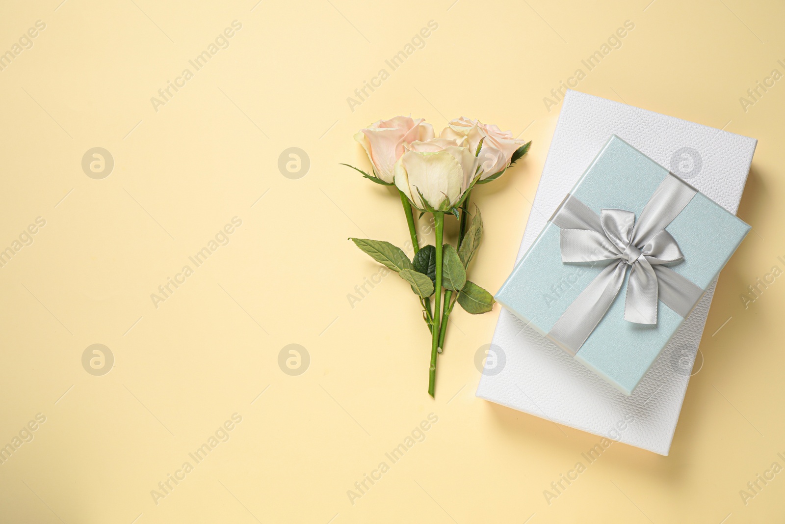 Photo of Elegant gift boxes and beautiful flowers on beige background, flat lay. Space for text