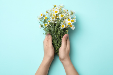 Photo of Woman holding chamomile bouquet on light background, top view