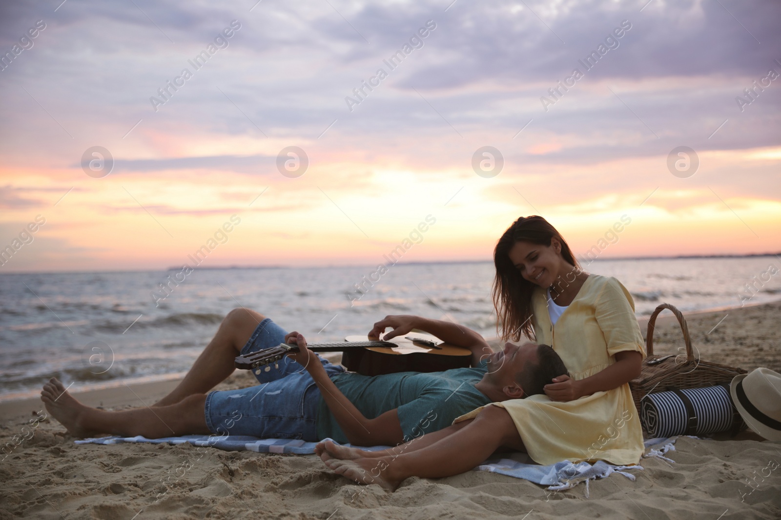Photo of Lovely couple with guitar and picnic basket on beach at sunset