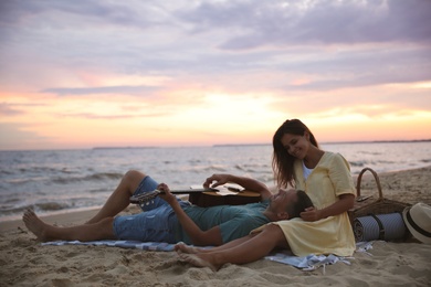 Lovely couple with guitar and picnic basket on beach at sunset