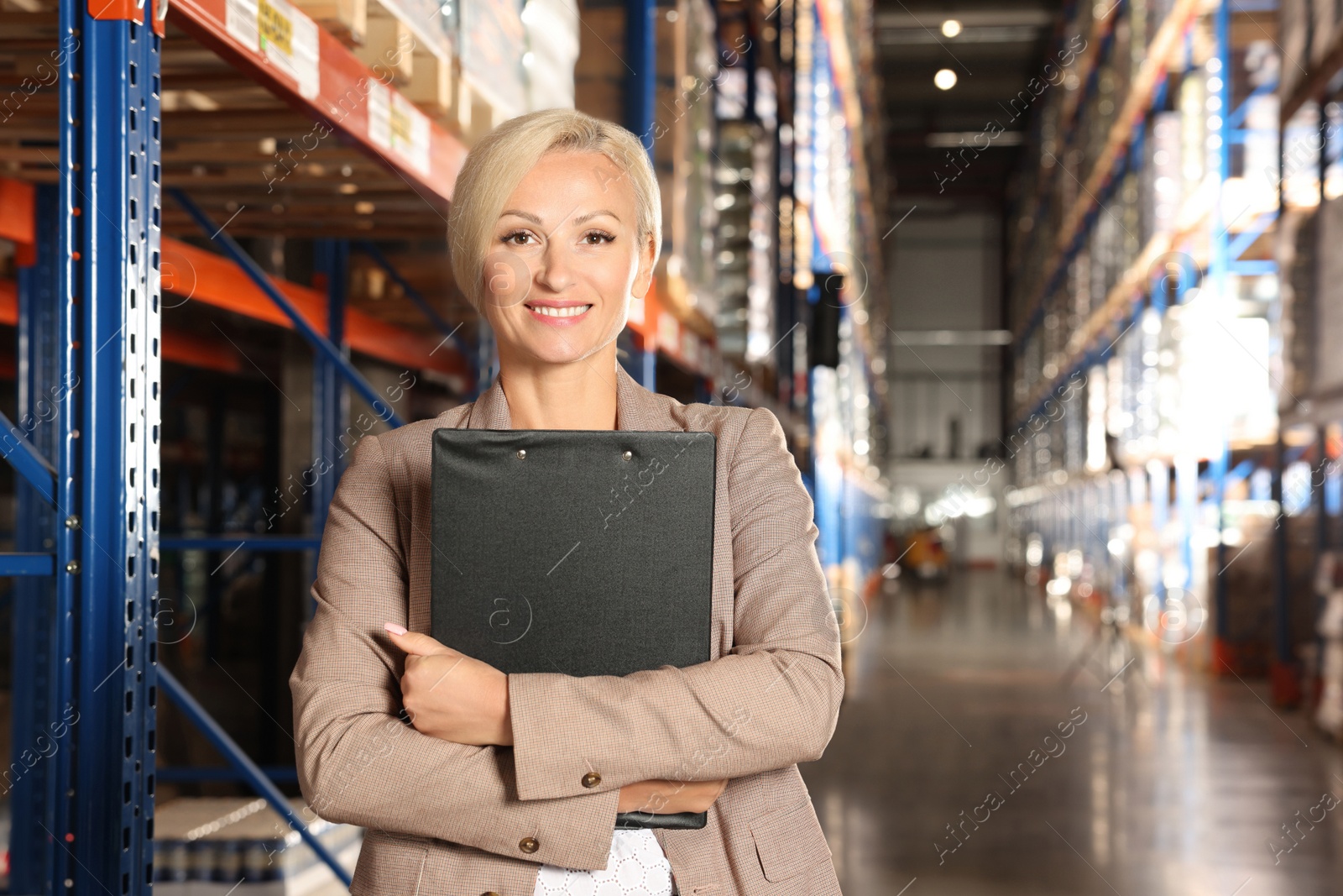 Photo of Happy manager holding clipboard in warehouse with lots of products. Space for text