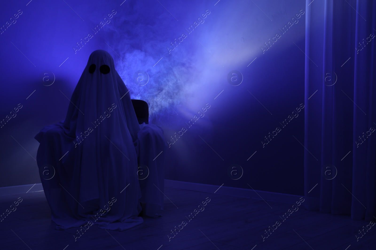 Photo of Creepy ghost. Woman covered with sheet sitting in armchair in blue light, space for text