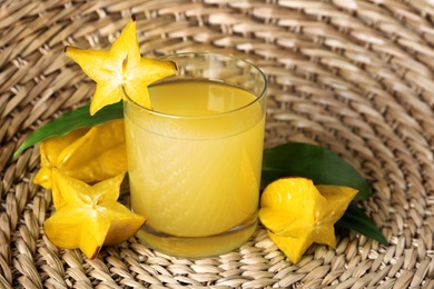 Photo of Delicious carambola juice and fresh fruits on wicker mat, closeup